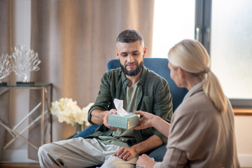 Man feeling thankful while taking napkins from psychologist