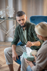 Bearded stylish man taking napkin while visiting psychologist