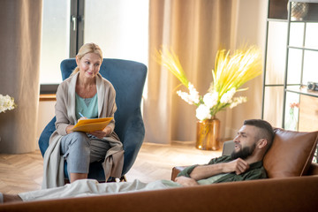 Bearded man lying on sofa and speaking with psychoanalyst