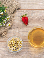 Glass cup of green tea with white chamomile flowers on wooden background.