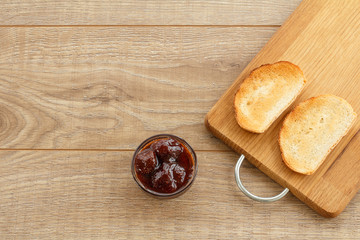 Homemade strawberry jam in bowl and toasts on wooden background.