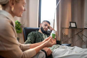 Bearded man looking at psychoanalyst holding pack of pills