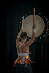 Fototapeta na wymiar Taiko drummer hits the big drum on stage on a black background, back view.