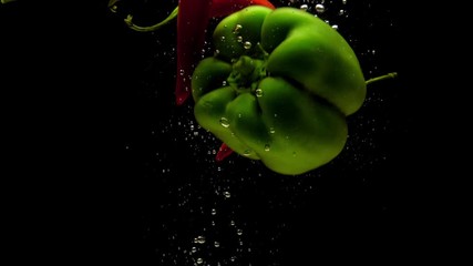 Red chili and green paprika falling in water on black background. Fresh organic vegetables splashing in aquarium. Grocery store, healthy food, diet, vegetarianism, air bubbles. Slow Motion. Close-up - Powered by Adobe