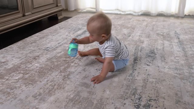 Active cheerful boy happily crawling in the room and taking his non-spill sippy cup from the floor. Happy childhood moments. Nursing child concept.