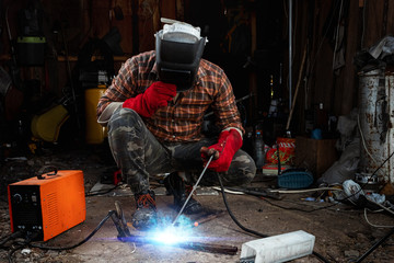 A male welder in a welding mask works with an arc electrode in his garage. Welding, construction,...