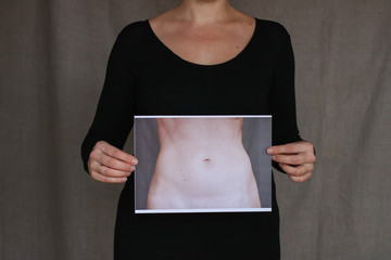 Ordinary woman wearing black clotes without head holding pictire with thin waist. Body issues...