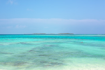 Wide angle picture of the Island on the horizon with bungalows on top of turquoise water in a island located close to Maafushi in Maldives. Picturesque seascape with blue sky.