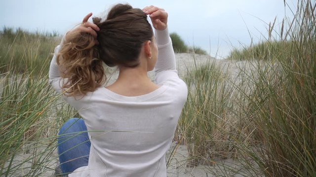 Young caucasian woman pulling her curly hair on Baltic coastline in dunes