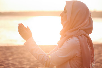 Obraz na płótnie Canvas Beautiful Muslim woman praying outdoors at sunset