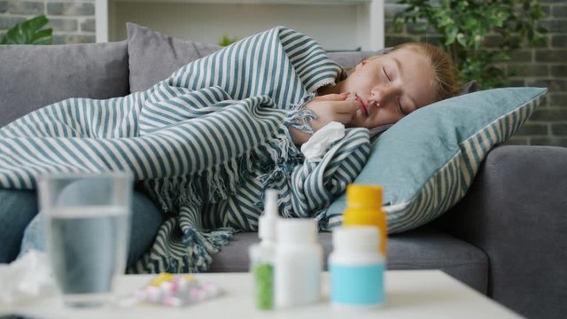 Slow motion of sick teenager taking body temperature with thermometer at home lying on couch with unhappy face. Medicine, lifestyle and healthcare concept.