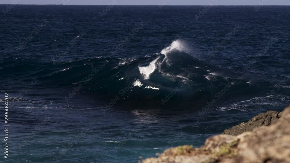 Poster a peaky wave breaks in an a frame shape not far from the rocky shore line. slow motion.