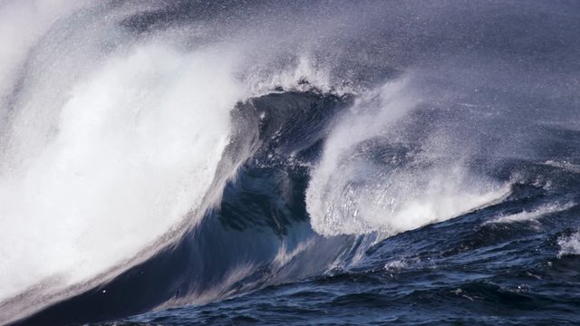 A glassy wave surges along a shallow rock shelf in slow motion while the offshore winds blow spray back up the wave face.