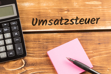 business desk with paper, pen and calculator and german text Umsatzsteuer, in english value added tax
