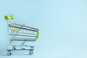 Empty small shopping cart on color background
