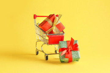 Small shopping cart with gift boxes on color background