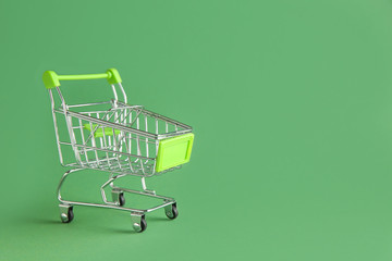 Empty small shopping cart on color background