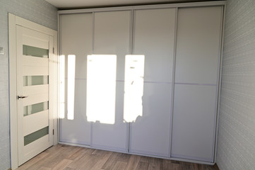 Photo of a white built-in wardrobe with sliding doors in a room with clear sun from the window.