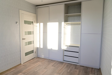 Photo of a white built-in wardrobe with sliding doors in a room with clear sun from the window.