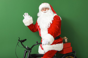 Santa Claus with Christmas gifts and bicycle on color background