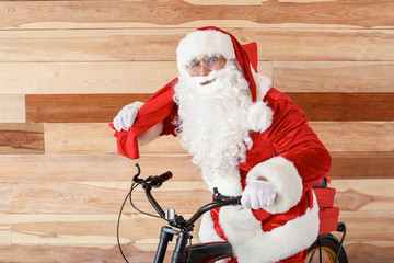 Santa Claus with Christmas gifts and bicycle near wooden wall