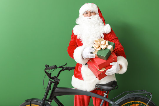 Santa Claus with Christmas gifts and bicycle on color background