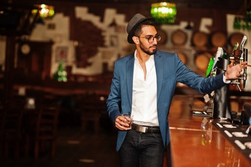 Handsome well-dressed arabian man with glass of whiskey and cigar posed at pub.