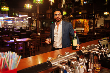 Handsome well-dressed arabian man with glass of whiskey and cigar posed at pub.