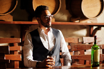 Handsome well-dressed arabian man with glass of whiskey and cigar posed at pub.