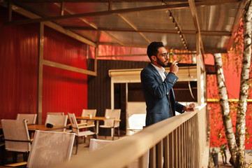 Handsome well-dressed arabian man smoke cigar with glass of whiskey at balcony of pub.