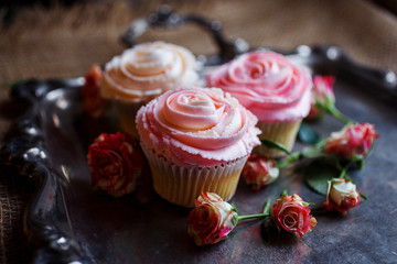 Beautiful creamy cupcakes on the silver tea tray decorated with roses