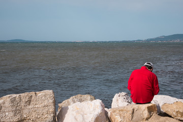 un homme triste assis au bord de la mer sur des rochers
