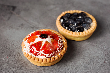Strawberry creamy tart and blueberry tatr on the gray background. Delicious summer dessert.