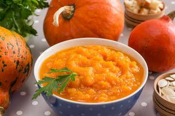 Pumpkin porridge in a bowl among orange pumpkins and seeds. Close-up.