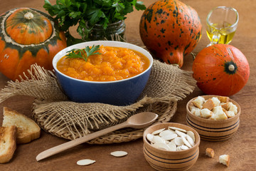 Pumpkin porridge in a bowl among orange pumpkins and seeds. Close-up.