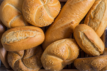 Bread and lots of fresh bread buns in a basket on a wooden table