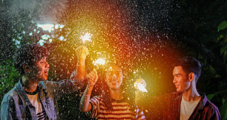 Asian group of friends having outdoor garden barbecue laughing with alcoholic beer drinks and showing group of friends having fun with sparklers on night