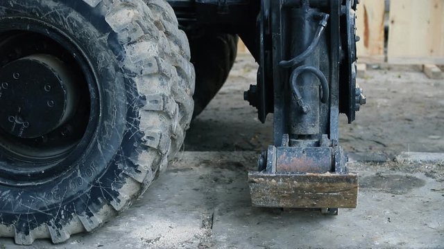 Close-up heavy industrial wheeled excavator extracting outrigger support balance arm for stabilization before moving ground at building construction site