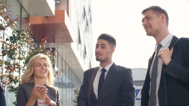 Medium shot of five young business colleagues of different ethnicities standing outdoors, discussing something and smiling