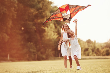 Summer sunny day. Mother and daughter have fun with kite in the field. Beautiful nature