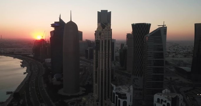 Aerial rising view of Doha iconic skyline at sunset, with the West Bay modern skyscrapers and towers, on the waterfront corniche