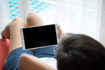 Beautiful Asian woman lie on day bed, use tablet computer to work from home and entertain herself during Covid-19 pandemic, spreading of virus, city lockdown and social distancing