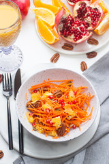 Healthy raw vegetarian salad with carrot, pomegranate seeds, oranges, pumpkin seeds, pecan nuts in grey bowl. Glass of orange juice and pomegranate on the background.
