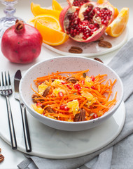 Healthy raw vegetarian salad with carrot, pomegranate seeds, oranges, pumpkin seeds, pecan nuts in grey bowl. Glass of orange juice and pomegranate on the background.