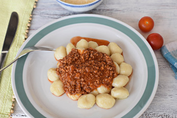 Potato gnocchi, Italian potato dumplings whit red meat sauce, cherry tomatoes at light wooden background