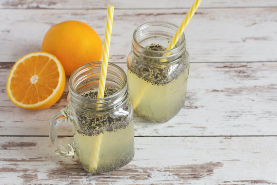 Chia seeds detox water. Healthy beverage with orange fruit slice in manson glass jars and drinking straw on wooden table with orange fruits.