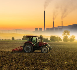 Tractor processing the field. Factory chimneys in the background