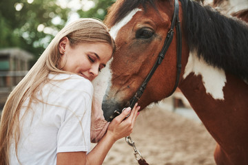 Cheerful blonde. Happy woman with her horse on the ranch at daytime