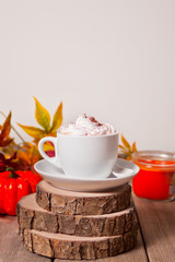 Cup of hot creamy cocoa with froth with autumn leaves and pumpkins on the background