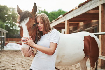 In white shirt. Happy woman with her horse on the ranch at daytime